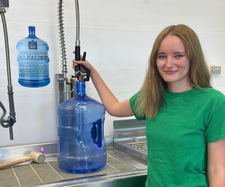 A blue water container sits amid greenery, glistening with water droplets in bright daylight.
